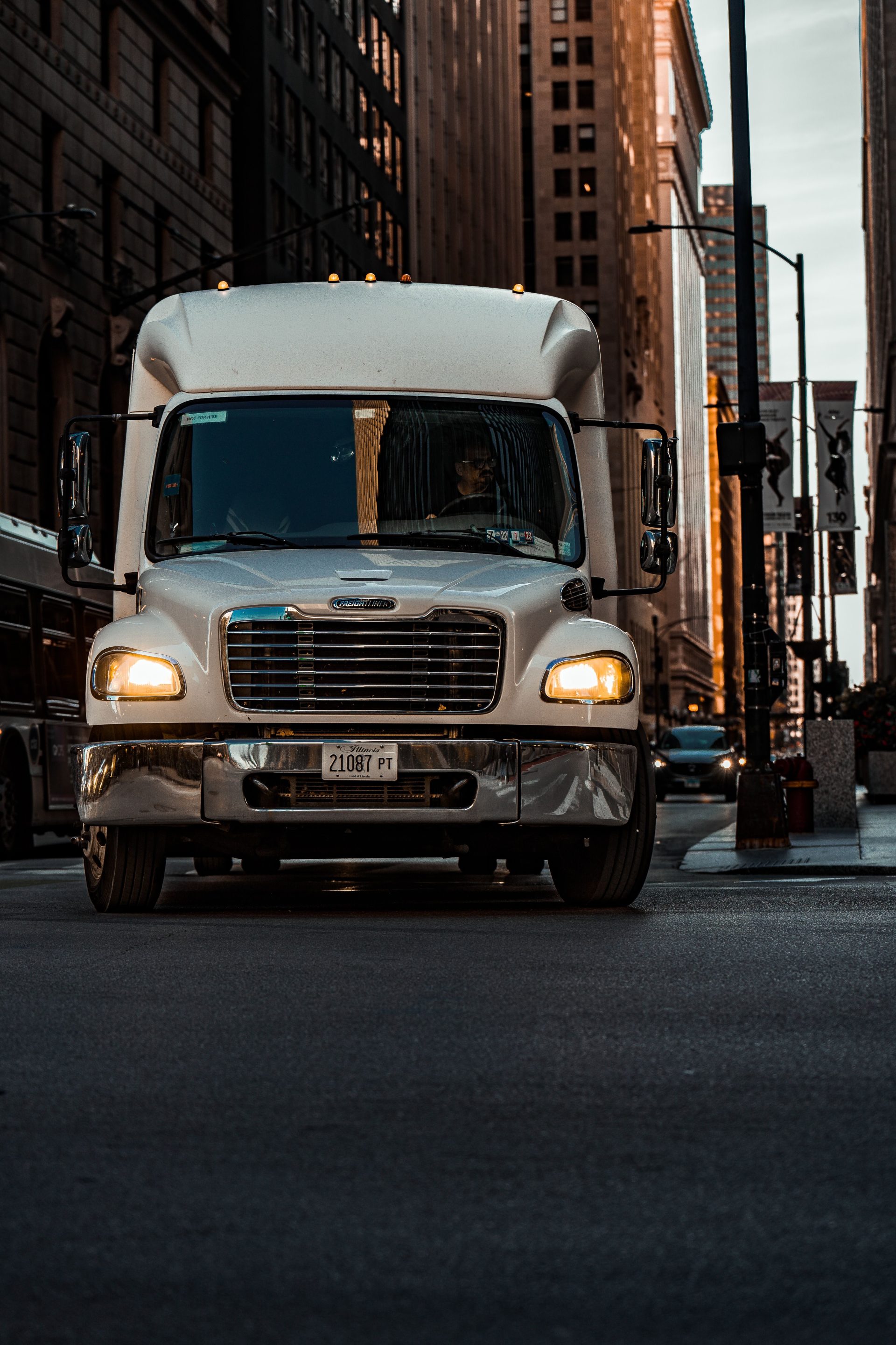 A delivery truck navigates a busy city street at dusk, capturing urban life.