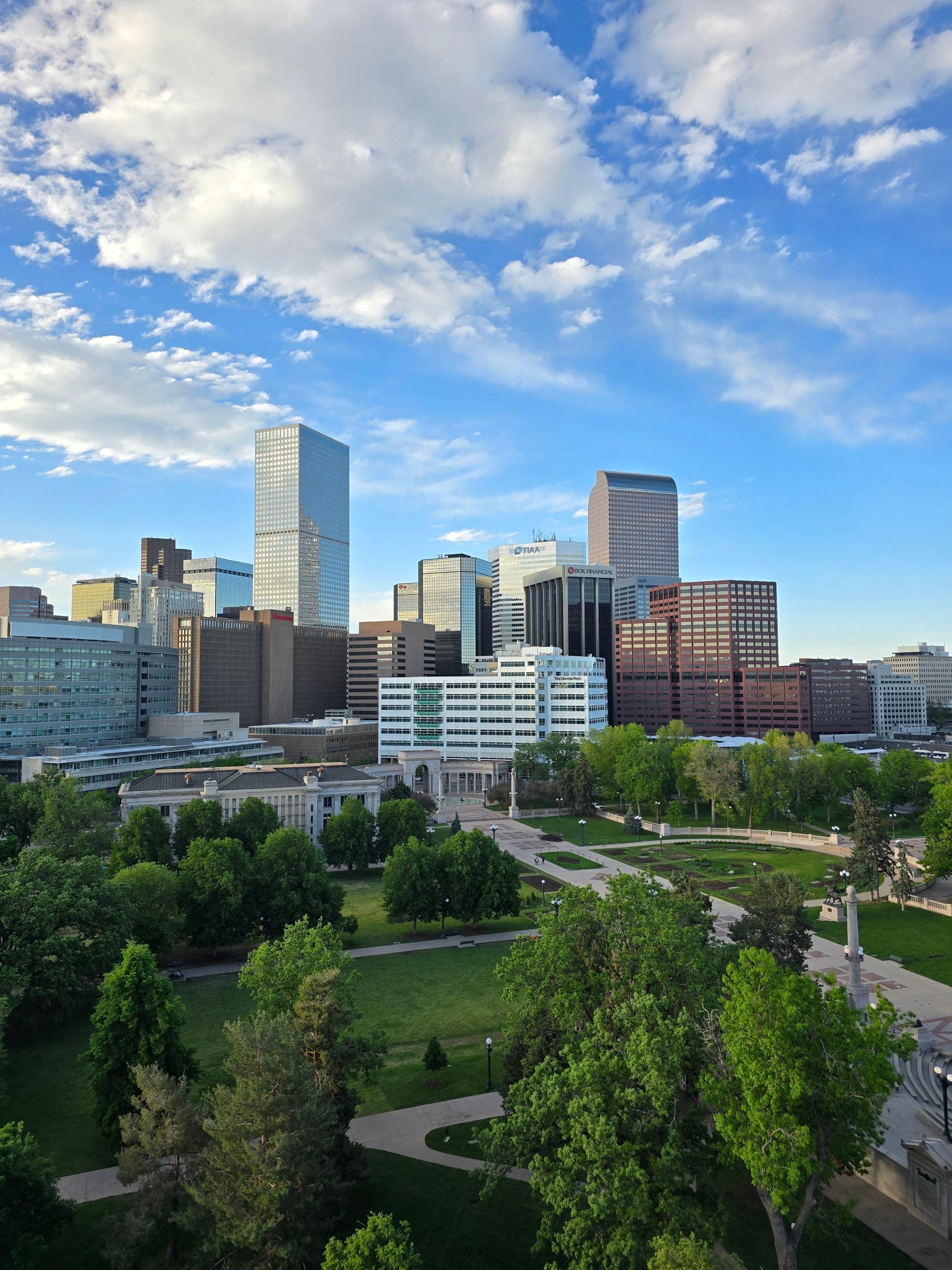 Scenic aerial view of the Denver skyline with lush green parks and skyscrapers under a blue sky.